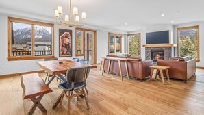 A spacious living area with a fireplace, large windows, and a dining table. - Spring Creek Vacations 2 BR Premier Condo 203TM (Canmore)