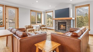 A spacious living area with leather sofas, a fireplace, and large windows offering mountain views. - Spring Creek Vacations 2 BR Premier Condo 203TM (Canmore)