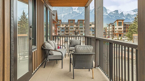 A balcony with wicker furniture and a view of mountain buildings. - Spring Creek Vacations 2 BR Premier Condo 203TM (Canmore)
