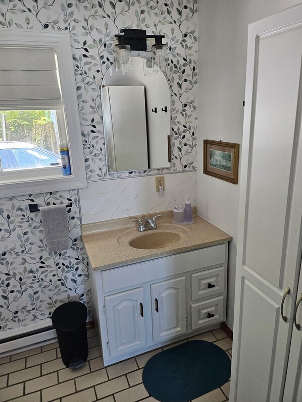Un baño con lavabo, espejo y ventana, con una toalla colgada en la puerta.