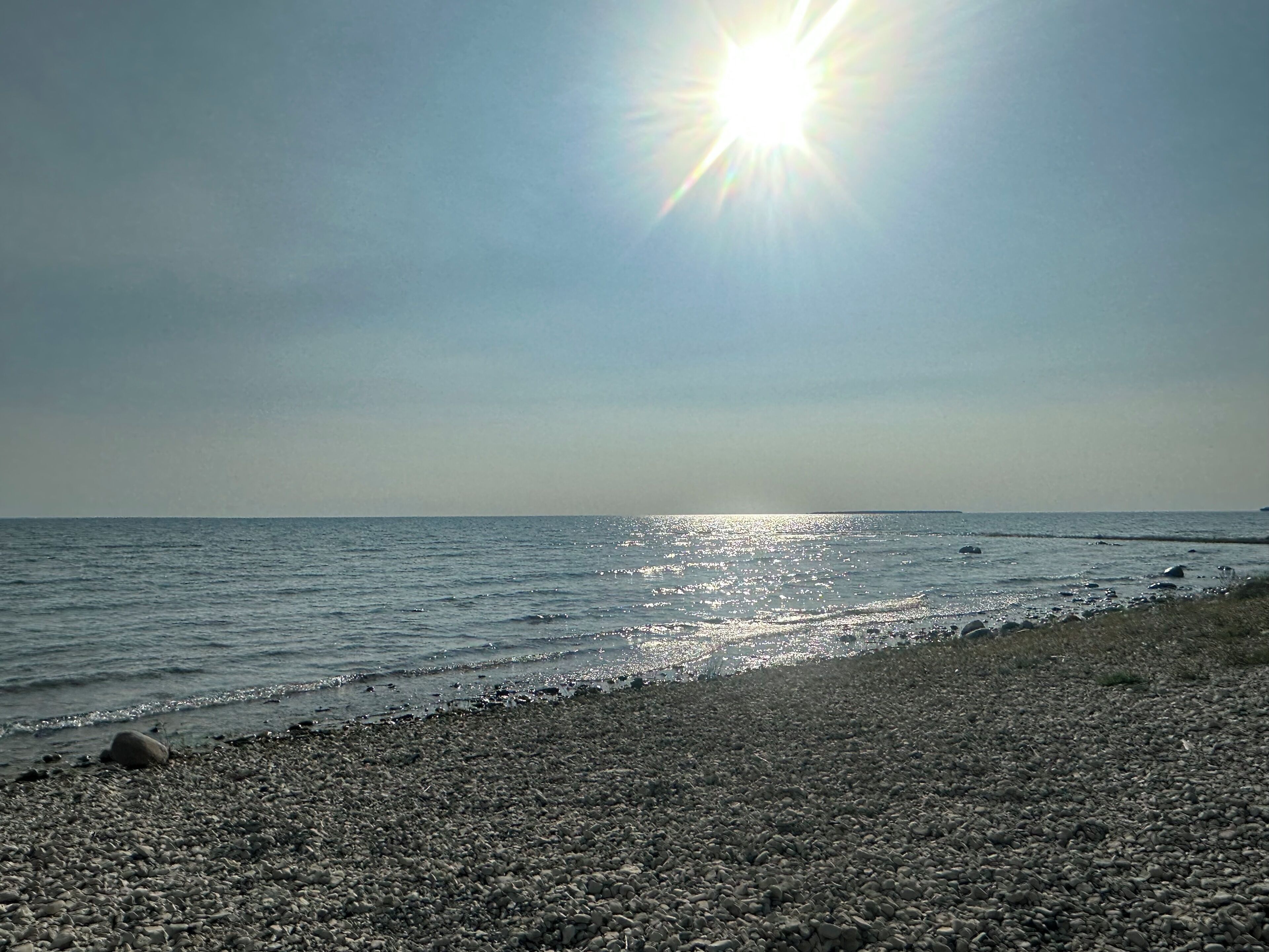 A pebbled beach with the sun shining over the water.