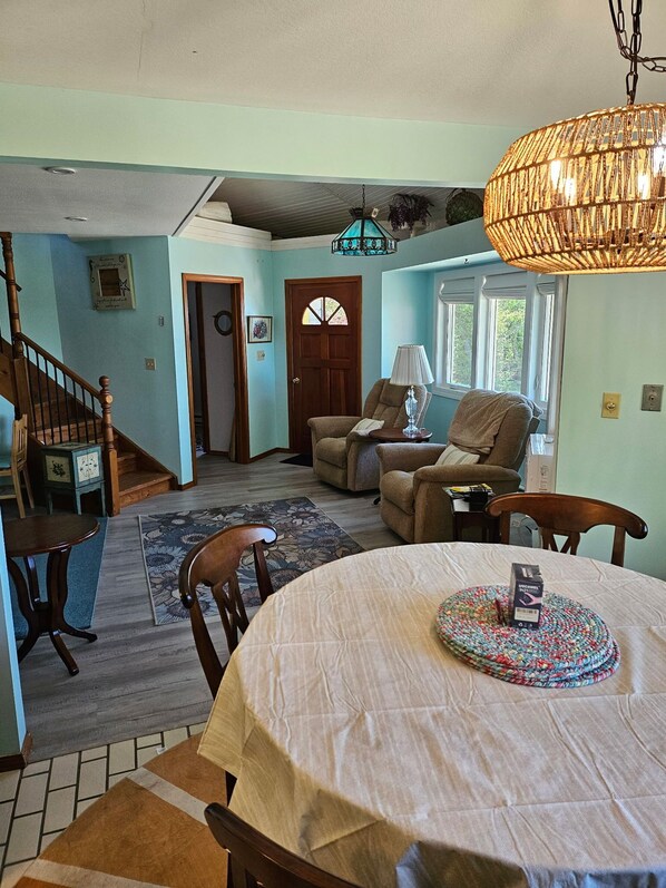A dining area with a round table, chairs, a patterned rug, and a hanging light fixture.