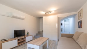 Een moderne woonkamer met een televisie, een houten salontafel en een bank. Er is een trap die leidt naar een keuken.