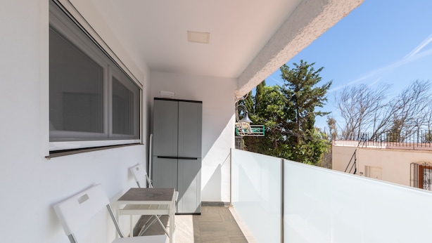 Een balkon met een witte stoel, een klein tafeltje en een raam.