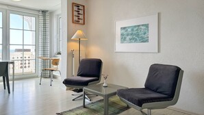 A modern living room with two armchairs, a small table, a floor lamp, and a large window with a view.