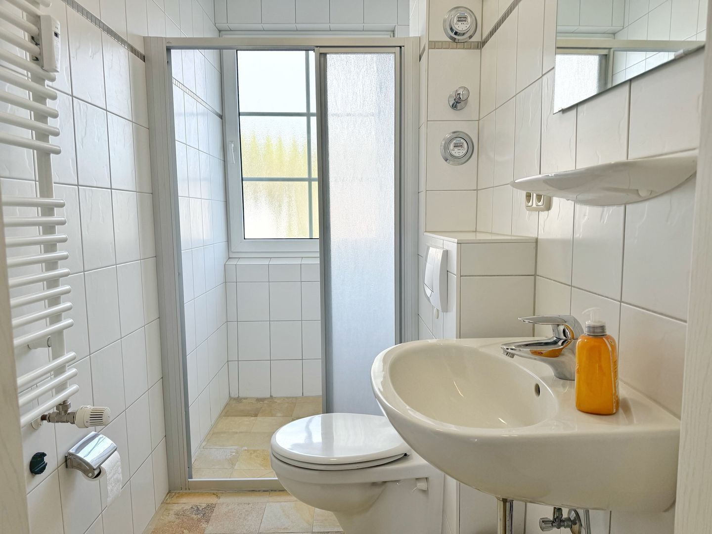 Et lille badeværelse med toilet, håndvask, et vindue og et håndklædetørrestativ.