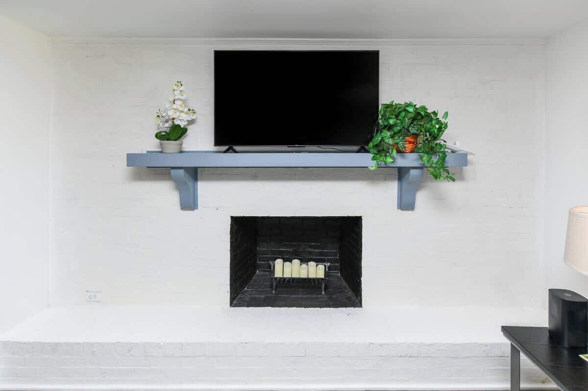 A fireplace with a TV above it, a shelf with plants, and a lamp on the right.