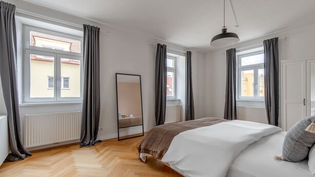 A bedroom with a large bed, a mirror, and a window with curtains.
