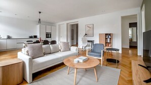 A modern living room with a sofa, coffee table, and armchair, a kitchen in the background, and a dining area.