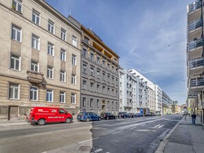 Une rue bordée d’immeubles à plusieurs étages, avec un camion rouge et des voitures garées.
