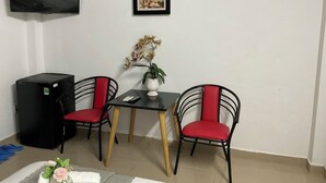 A small room with a TV mounted on the wall, a table with two chairs, a small black refrigerator, and a framed picture above the table. - Minh Chau Hotel - Dien Bien Phu (Ho Chi Minh City)