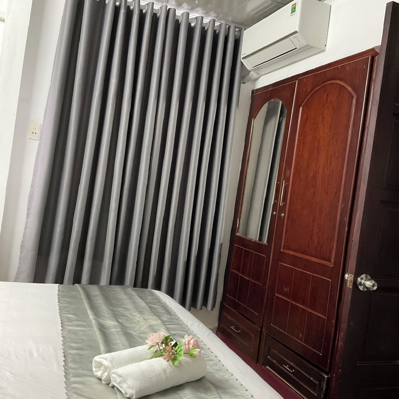 Ein Hotelzimmer mit einem Bett, grauen Vorhängen, einem Holzschrank und einer Klimaanlage.
