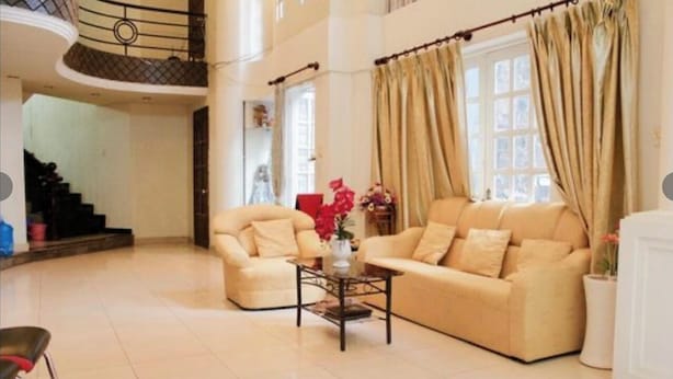 A spacious living area with a beige sofa set, a coffee table with a vase, and a staircase leading to an upper level. - Minh Chau Hotel - Dien Bien Phu (Ho Chi Minh City)