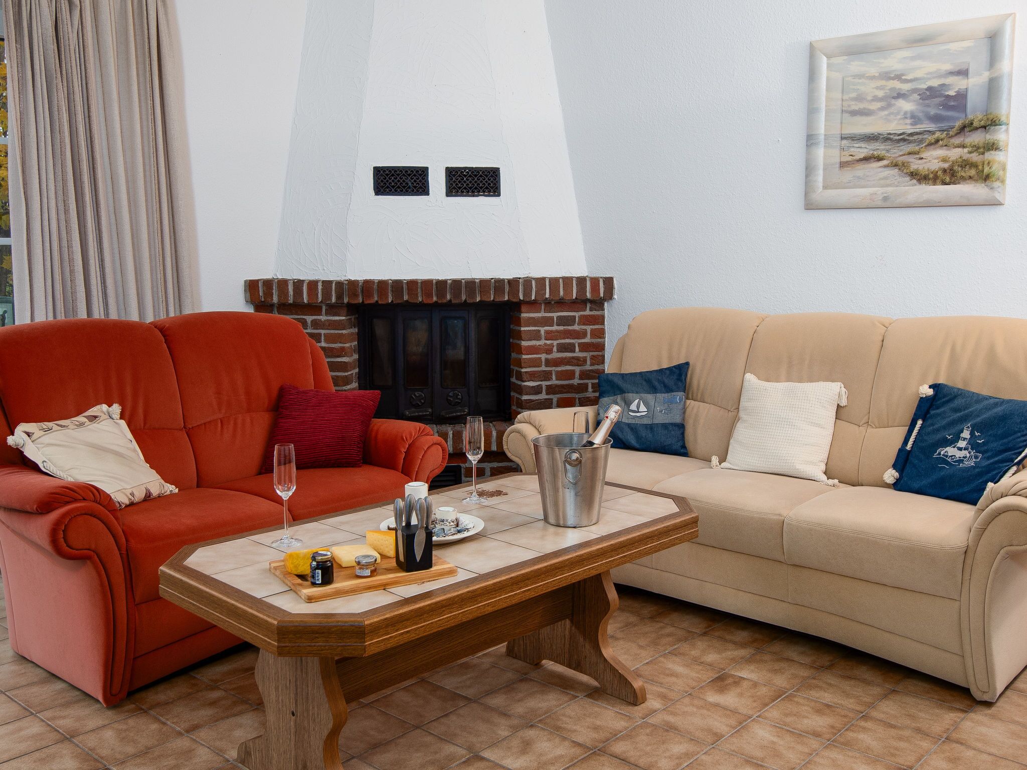 Ein Wohnzimmer mit Kamin aus Ziegelsteinen, zwei Sofas, einem Holztisch mit Speisen und Getränken sowie einem gerahmten Landschaftsbild an der Wand.