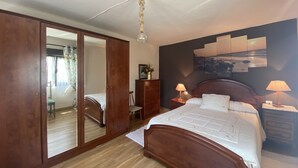 A bedroom with a wooden bed, a wardrobe, a mirror, a nightstand with a lamp, and a wall with a painting. - Vivienda Vacacional La Mata Vieja (La Franca)