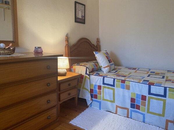 Un dormitorio con un aparador de madera, una lámpara de noche, una cama con colcha colorida y un cuadro enmarcado en la pared.