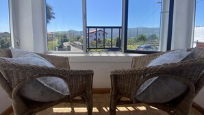 A room with two wicker chairs facing a large window overlooking a road and buildings. - Vivienda Vacacional La Mata Vieja (La Franca)