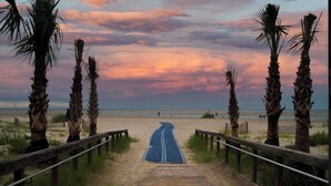 Ein Holzsteg führt zu einem Strand, gesäumt von Palmen.