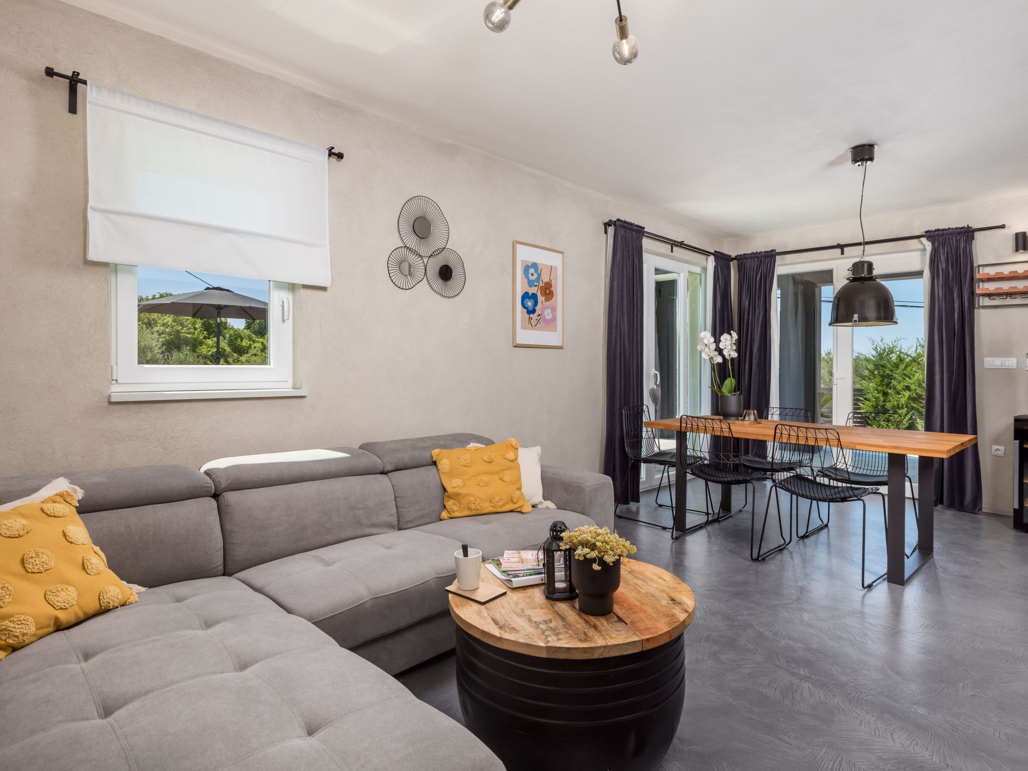 Una sala de estar moderna con un sofá seccional gris, una mesa de centro de madera y un comedor con una mesa de madera y sillas negras.