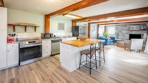 A modern kitchen with a central island, wooden beams, and a stone fireplace. - Beach Daze Duplex - Unit B! Fenced-in backyard! Pets Welcome! 5 Blocks to beach! (Carolina Beach)