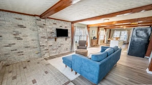 A spacious living area with a brick wall, a flat-screen TV, a blue sofa, and a wooden floor. - Beach Daze Duplex - Unit B! Fenced-in backyard! Pets Welcome! 5 Blocks to beach! (Carolina Beach)