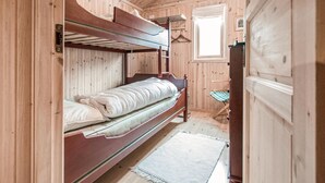 Een houten kamer met stapelbedden, een klein raam en een houten garderobe.