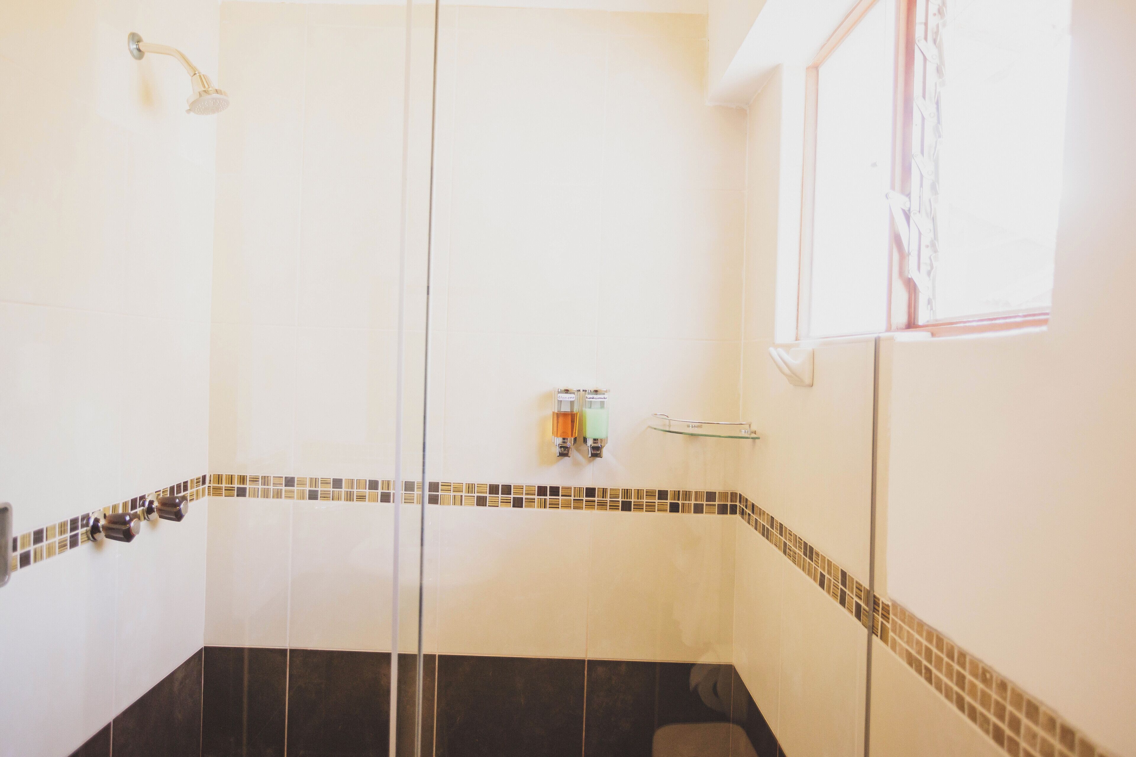 A bathroom with a glass shower enclosure, a hand dryer, and a towel rack.