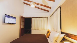Een hotelkamer met een bed, een aan de muur bevestigde televisie, een raam met gordijnen en een plafondventilator.