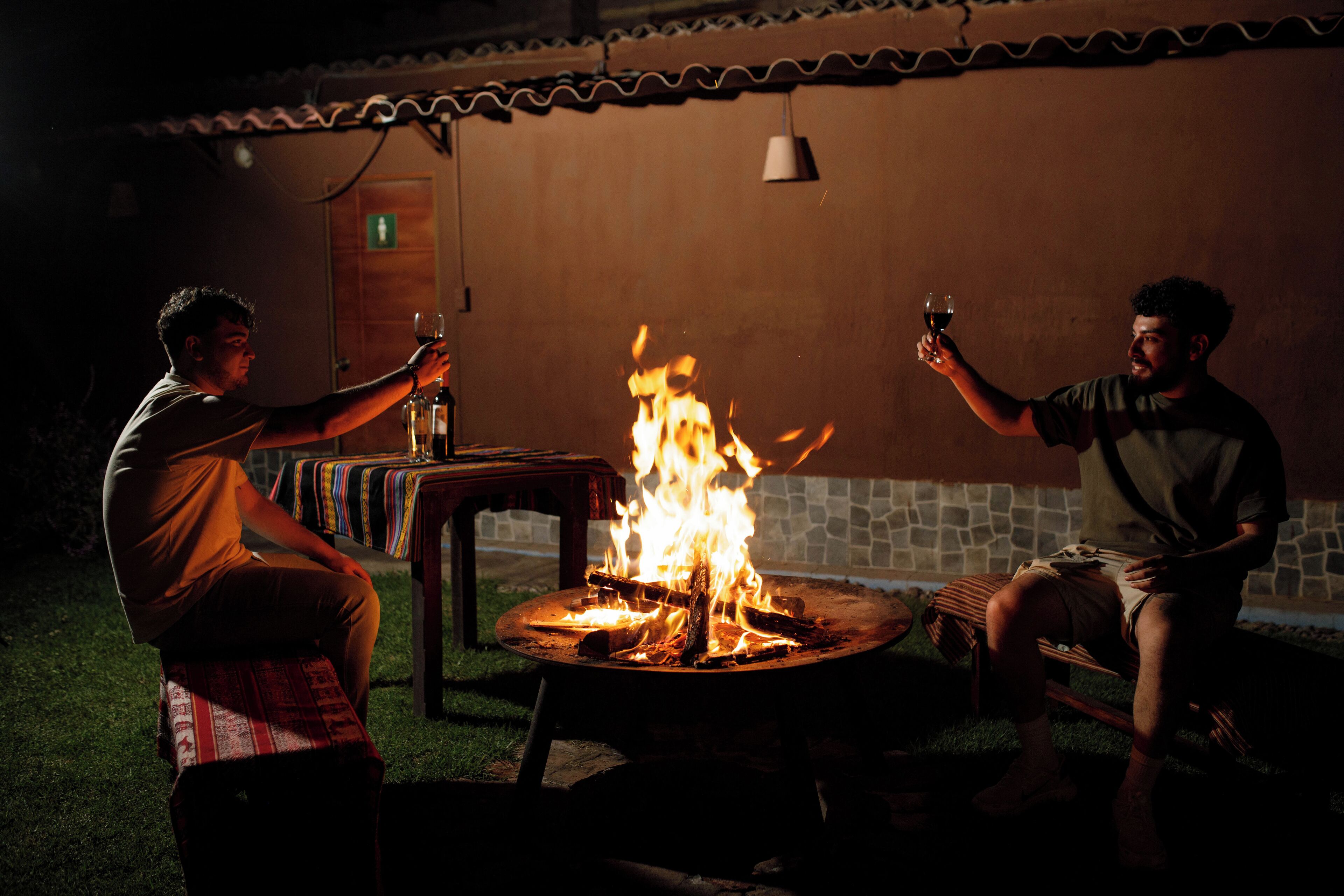 Two people sitting outdoors at a campfire with a table and chairs.