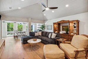 A spacious living area with a dark-colored sectional sofa, a round coffee table, a beige armchair, and a wooden cabinet.