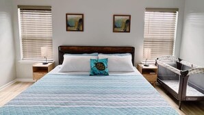 A bedroom with a bed, a ceiling fan, two windows with blinds, and two wall-mounted paintings. - Coastal Oasis: Games, Pool, BBQ & beach (Myrtle Beach)