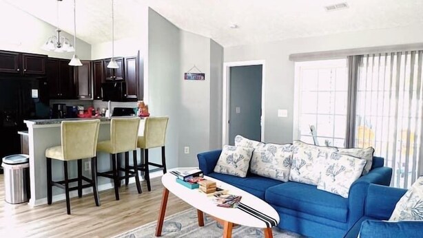 A modern living room with a blue sofa, a coffee table, and a ceiling fan. - Coastal Oasis: Games, Pool, BBQ & beach (Myrtle Beach)
