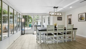 A dining area with a glass-enclosed patio, a chandelier, and a dining table with chairs.
