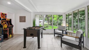 A spacious room with a foosball table, a retro arcade machine, and a large window offering a view of the outdoors.