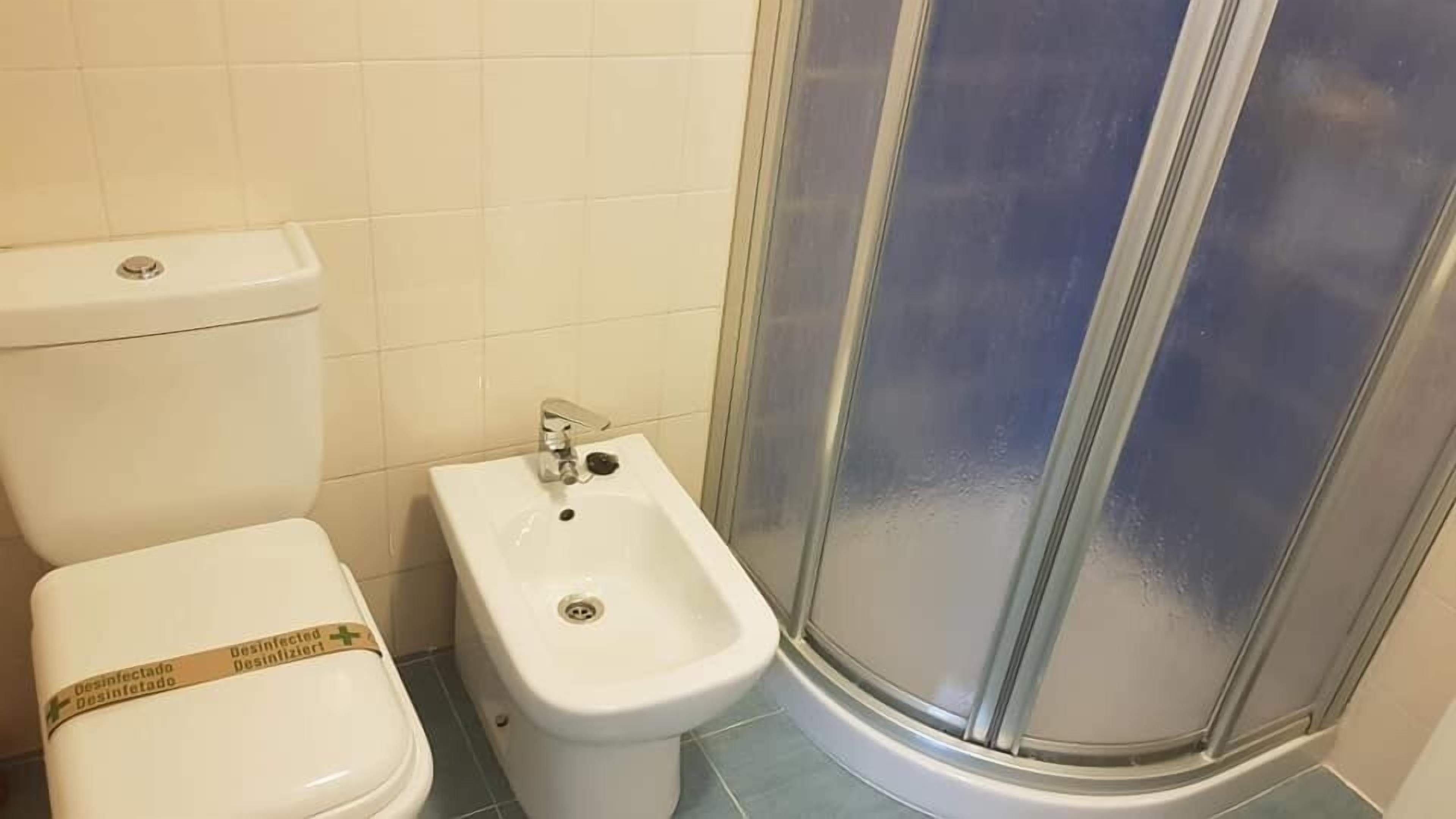 A bathroom with a toilet, bidet, and glass-enclosed shower.
