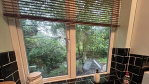 A bathroom with a window, black tiled walls, a toilet, and a sink with a faucet. - Cosy and secluded brook-side lodge (Sleaford)