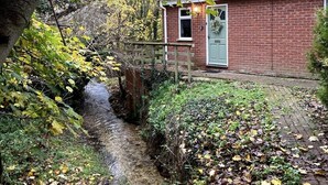 A house with a brick exterior, a small front yard, and a narrow stream running through it. - Cosy and secluded brook-side lodge (Sleaford)