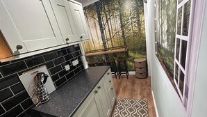 A kitchen with white cabinets, black tiles, a wooden countertop, a stove, and a window with a forest mural. - Cosy and secluded brook-side lodge (Sleaford)