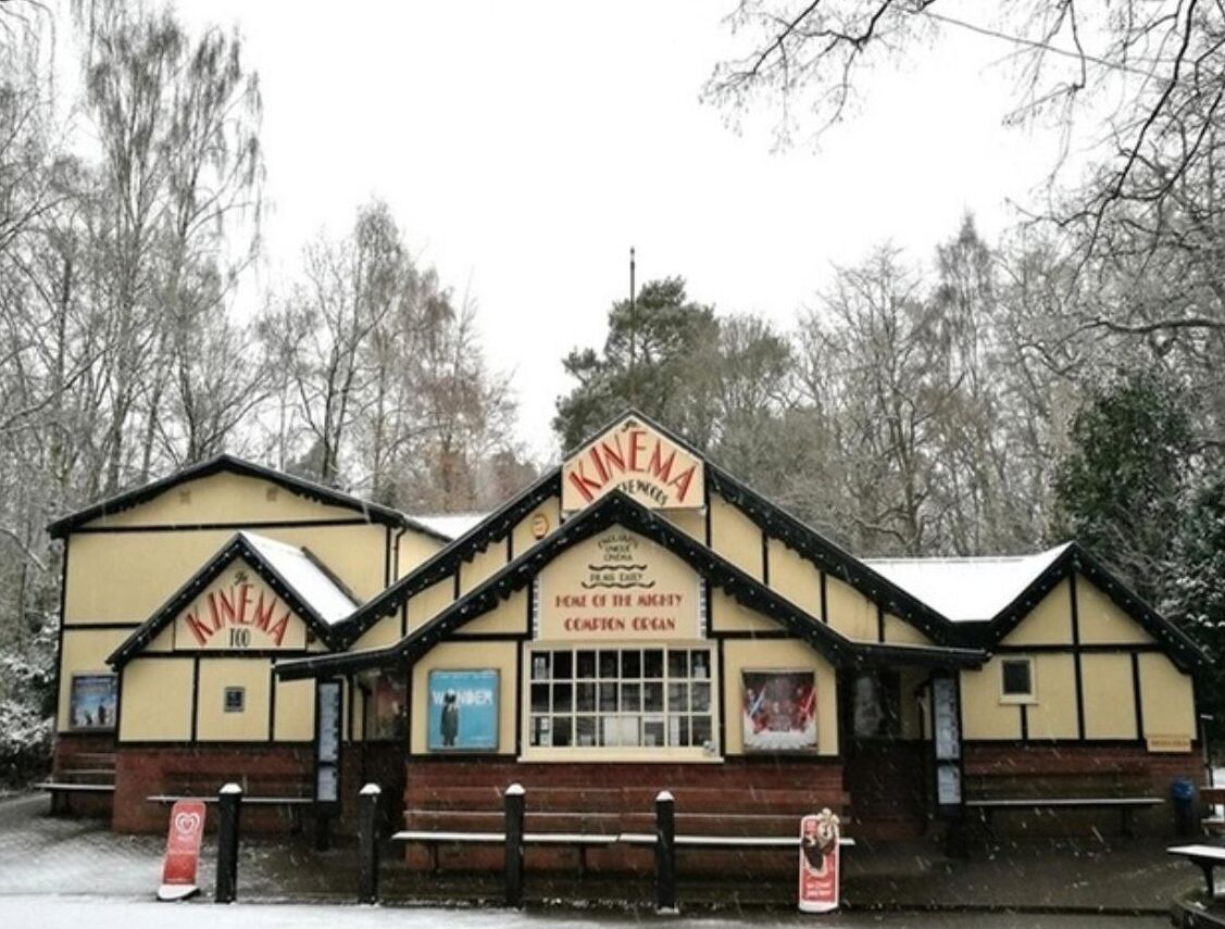 A cinema with a traditional design, featuring a marquee and a sign that reads 'KINEMA 100.'