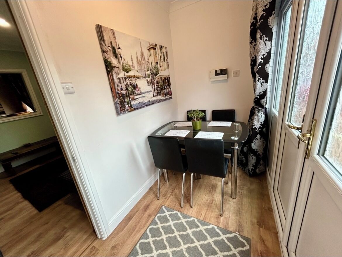 Un comedor con una mesa dispuesta para cuatro personas, un cuadro en la pared y una ventana con cortinas.