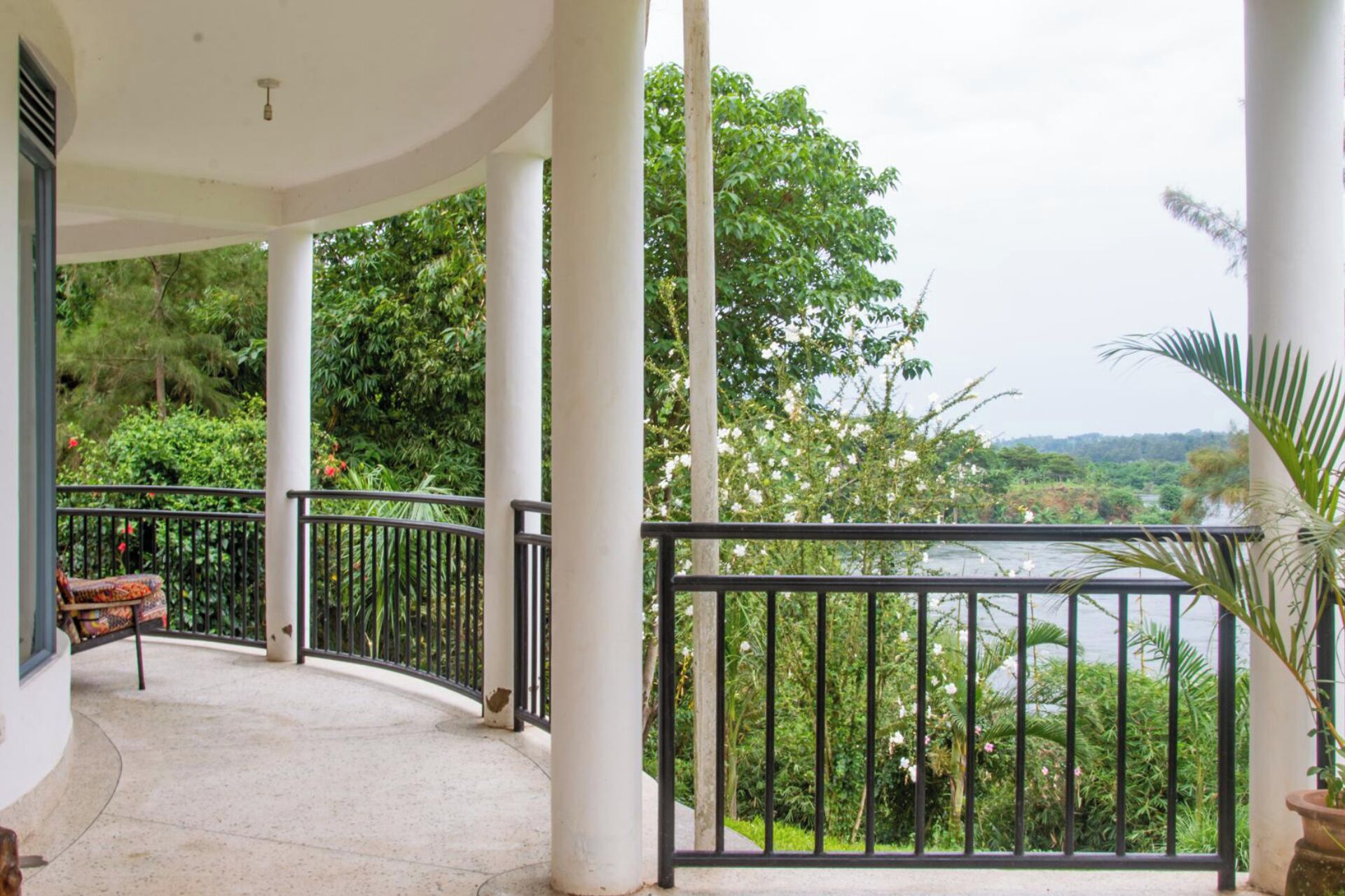 A covered balcony with a curved railing, white columns, and a view of lush greenery and a river.