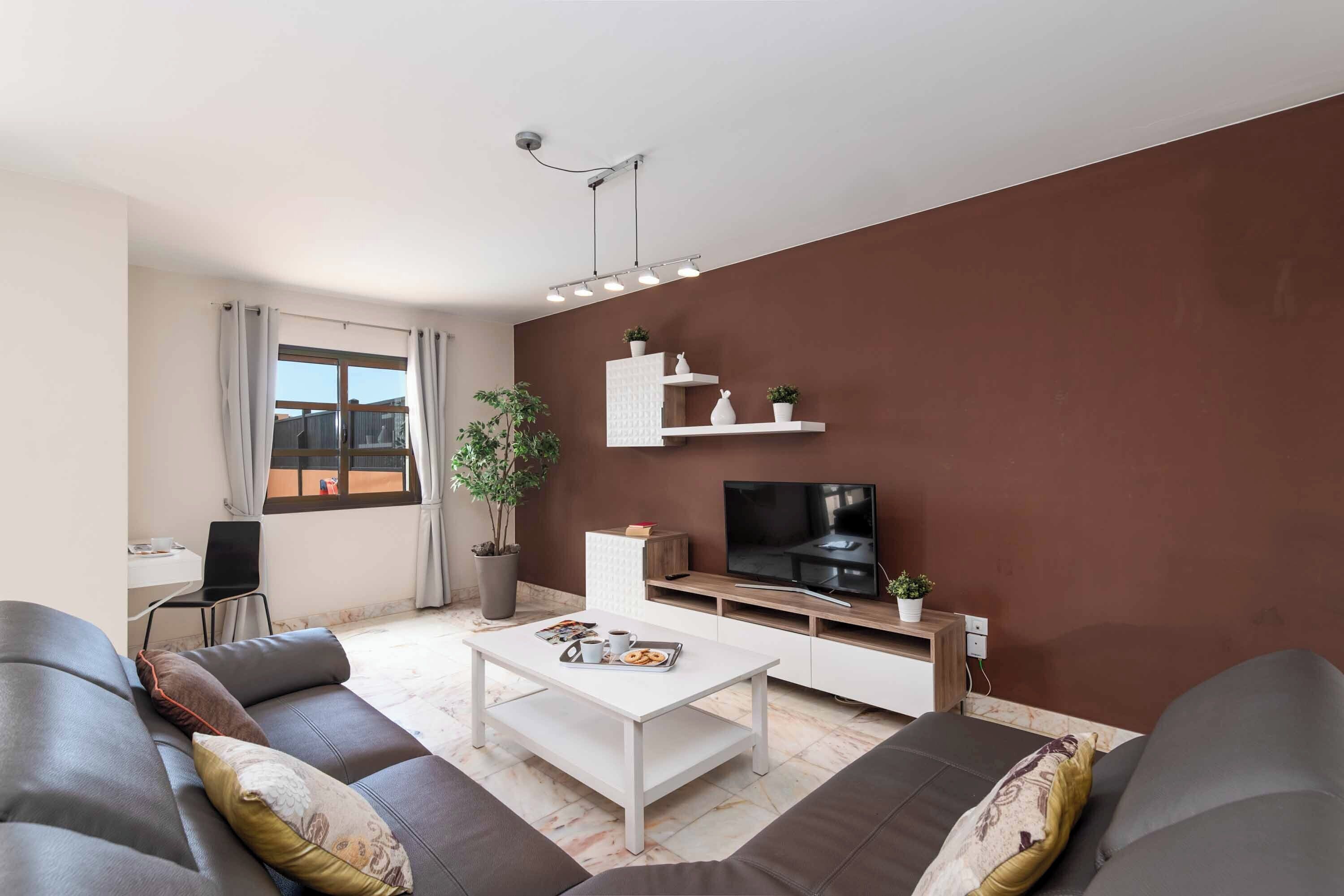A modern living room with a sofa, coffee table, TV, and a small kitchen area.