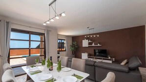 A modern dining area with a white table set for four, a sofa, and a TV in the background. - Vista Lobos (La Oliva)