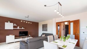 A modern living room with a grey sofa, a TV, a dining table set for four, and a wooden door. - Vista Lobos (La Oliva)