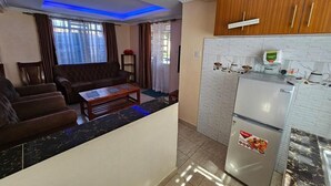 Una sala de estar con un sofá, una mesa de centro y un área de cocina con refrigerador y armarios.