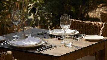 An outdoor dining table set with plates, cutlery, and glasses, surrounded by wicker chairs.