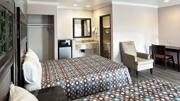 A hotel room with a large bed, a desk, a chair, and a small kitchenette. - HYLAND MOTEL (La Habra)