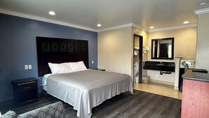 A hotel room with a bed, a desk, a chair, a mirror, and a patterned sofa. - HYLAND MOTEL (La Habra)