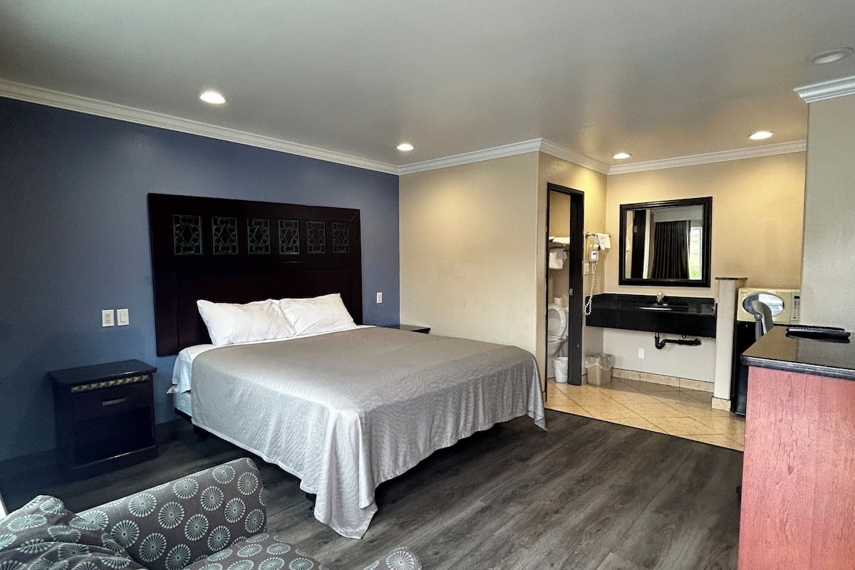 A hotel room with a bed, a desk, a chair, a mirror, and a patterned sofa.