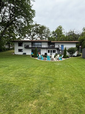 A two-story house with a front deck, a blue door, and a small garden area with outdoor furniture.